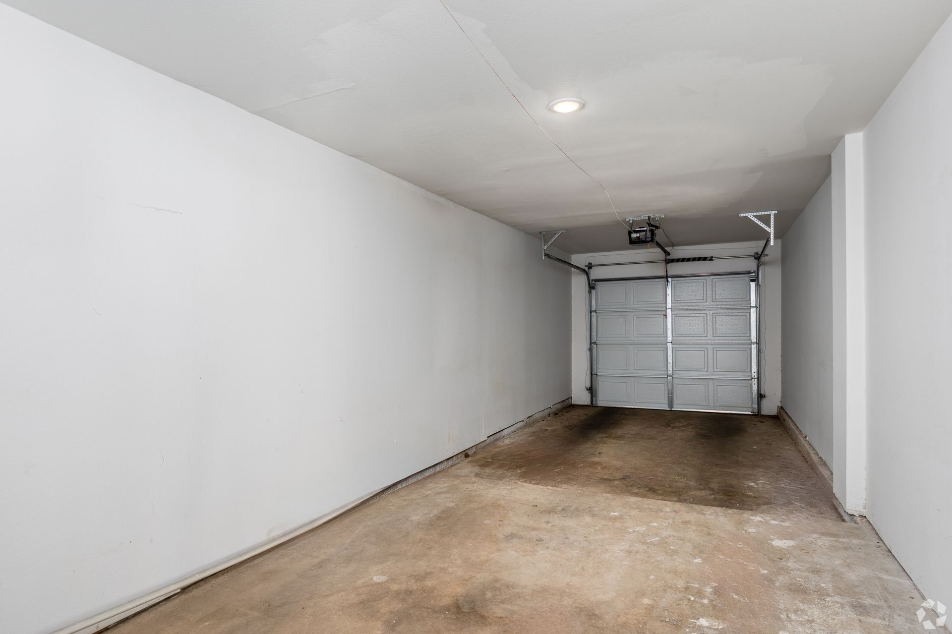 Empty, concrete-floored garage with open, white garage door. White walls and ceiling; some stains on the floor.