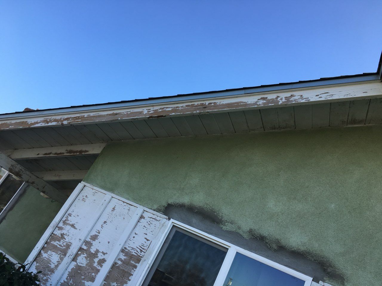 Exterior view of a house with peeling paint on the eaves and a green stucco wall.