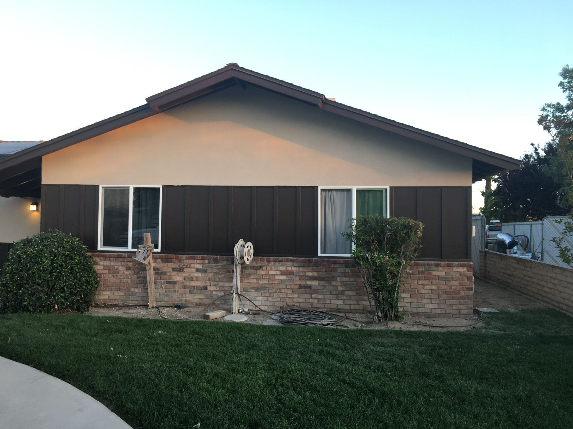 Exterior of a house: brown and tan siding, brick base, white-framed windows, green lawn.