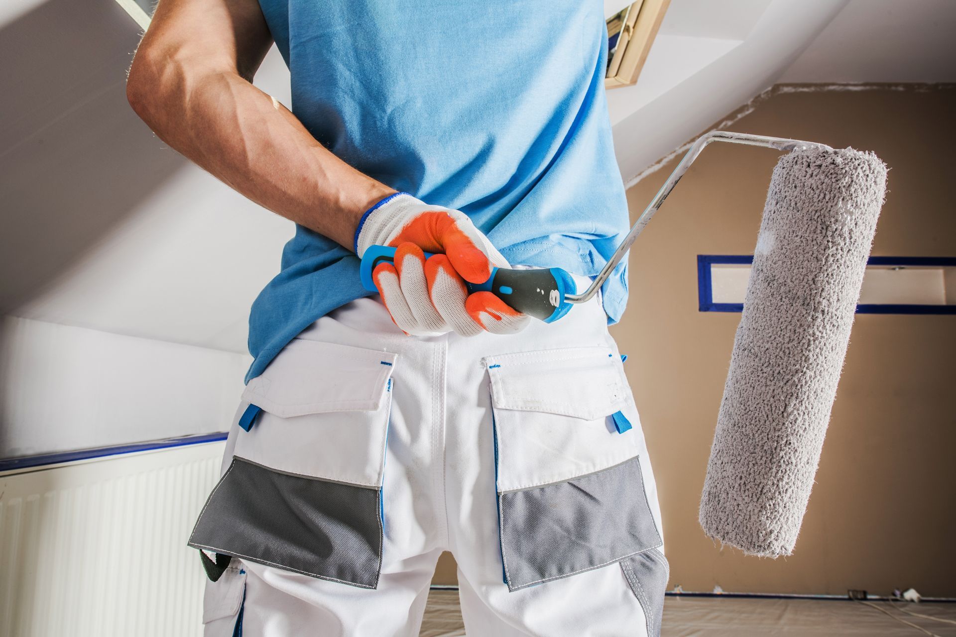 Painter holding a paint roller behind their back, wearing gloves and work pants.