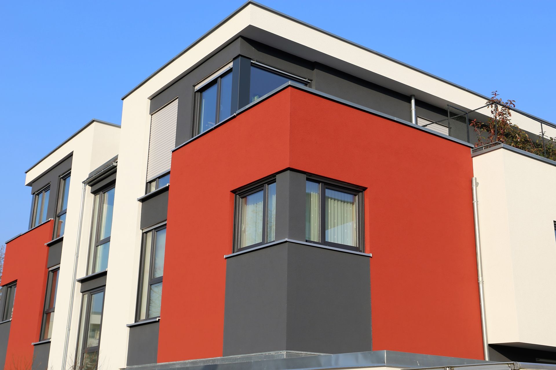 Modern building with white, red, and gray sections under a blue sky.