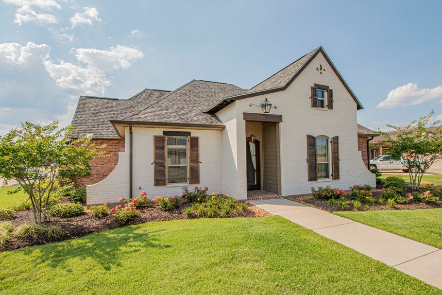 White stucco house with stone roof, front lawn, and walkway under a blue sky
