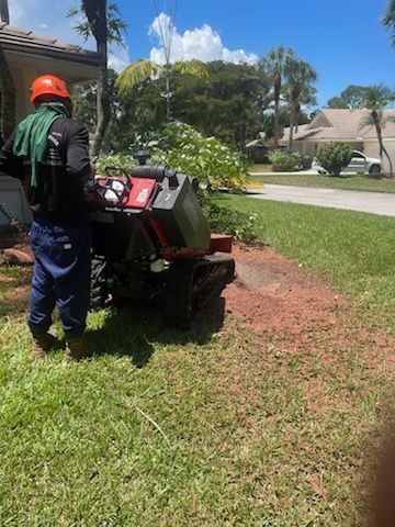 Firefighter using a chainsaw to cut a tree stump, with a crane truck nearby. Outdoors, sunny day.