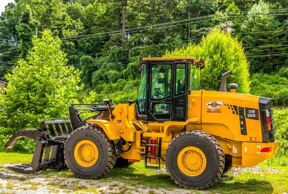 Yellow loader with black grapple in a grassy area with trees.