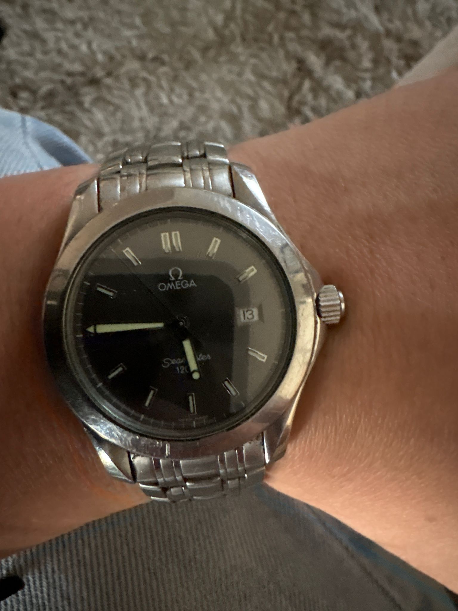 Een close-up van een zilverkleurig Omega Seamaster horloge met een zwarte wijzerplaat en datumvenster