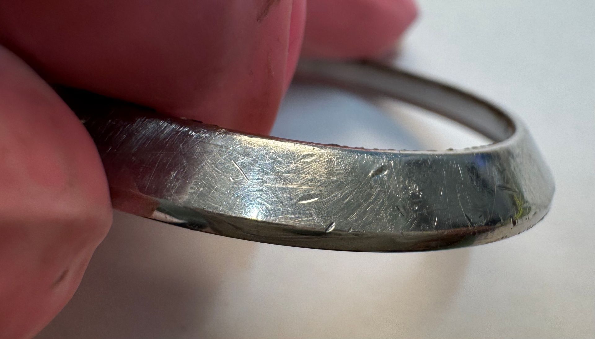 een dunne, schuine metalen ring vast met een versleten, bekrast en reflecterend zilverkleurig oppervlak.