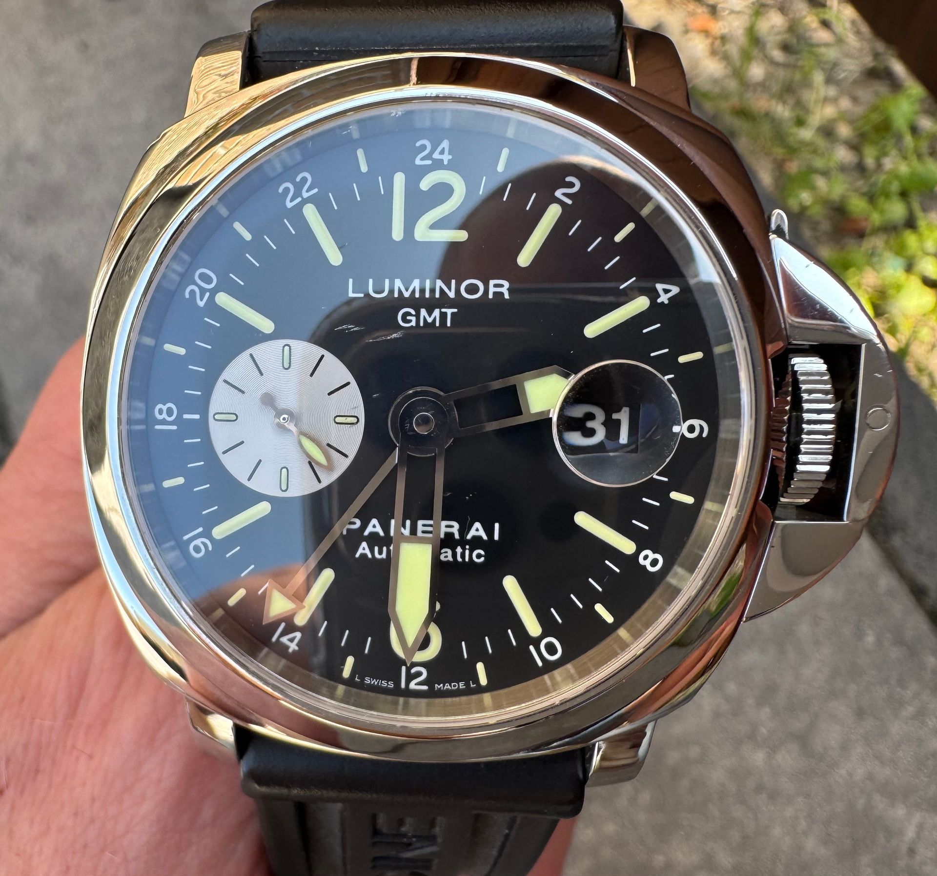 Detailopname van een zilverkleurig Panerai Luminor GMT-horloge met een zwarte wijzerplaat, datumvenster en rubberen band.