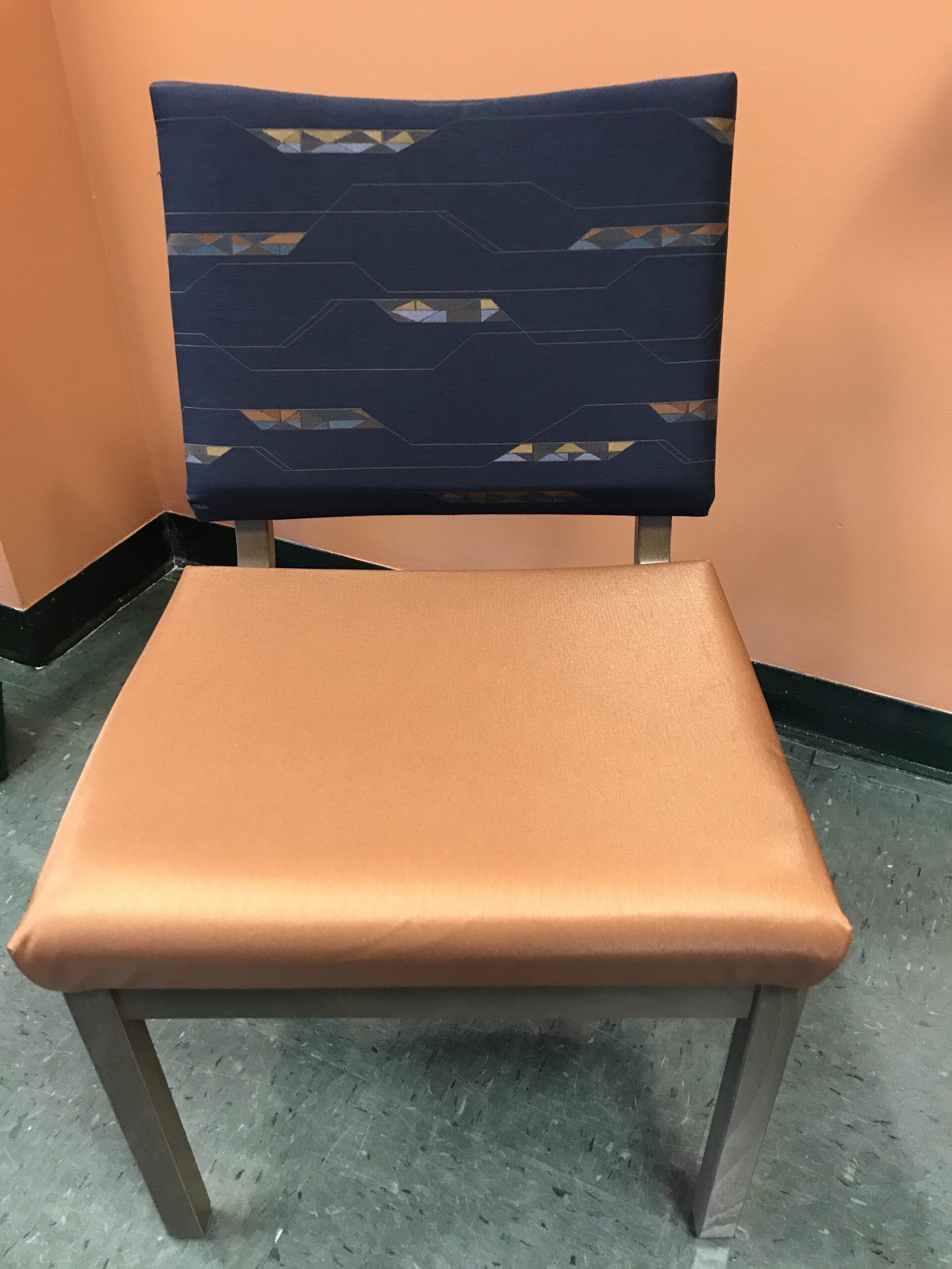 A chair with a blue back and a brown seat is sitting in front of a wall.
