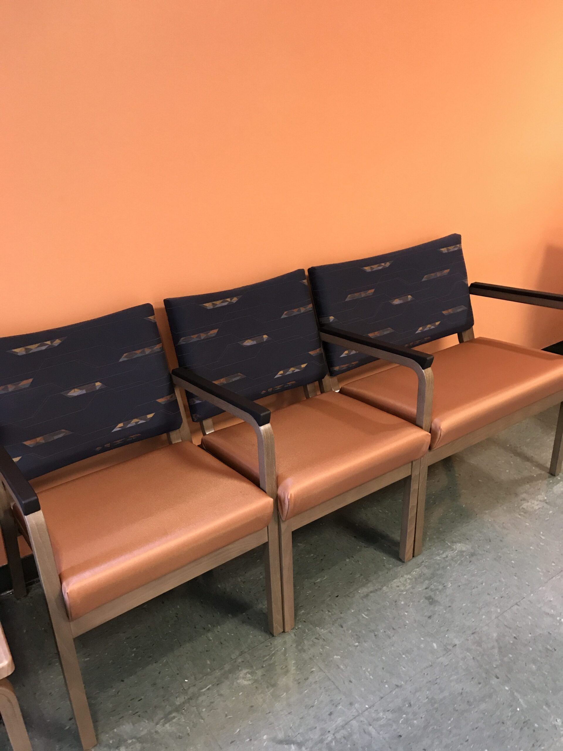 A row of chairs in a waiting room with an orange wall