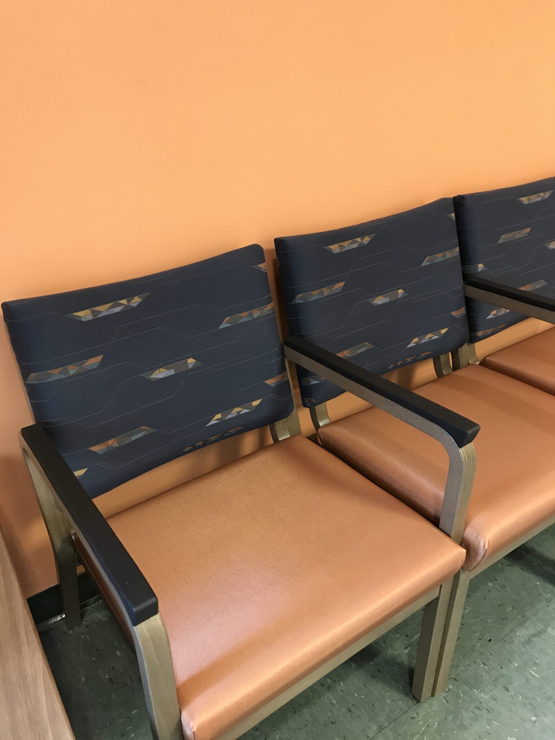 A row of chairs in a waiting room with an orange wall