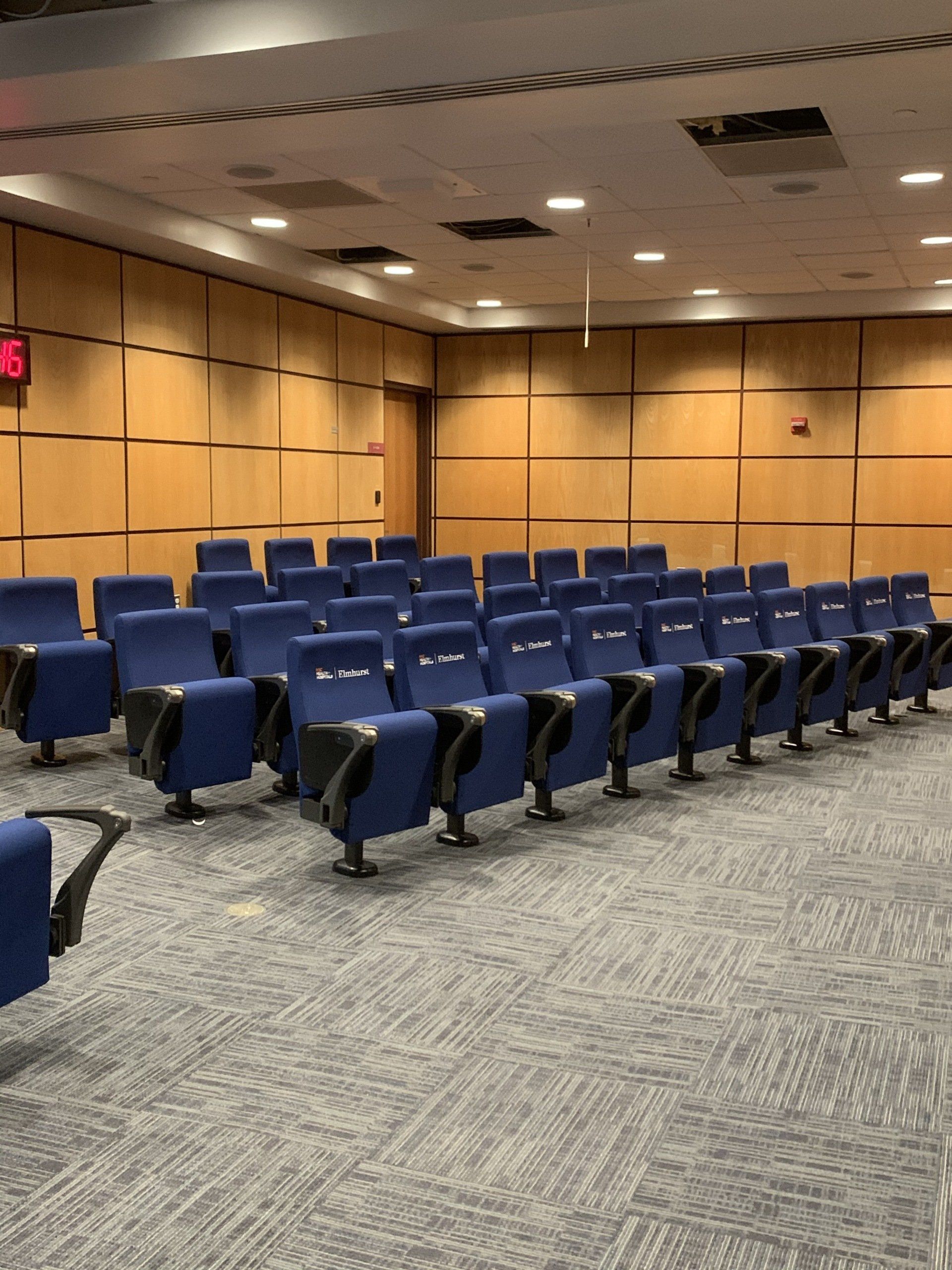 Rows of blue chairs in an auditorium with wood paneling