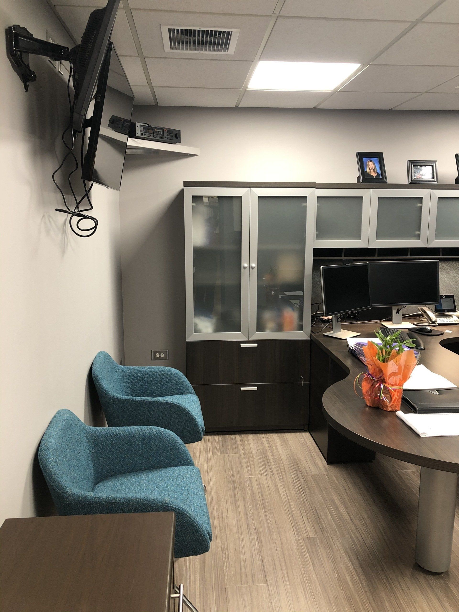 A waiting room with two blue chairs and a tv mounted on the wall
