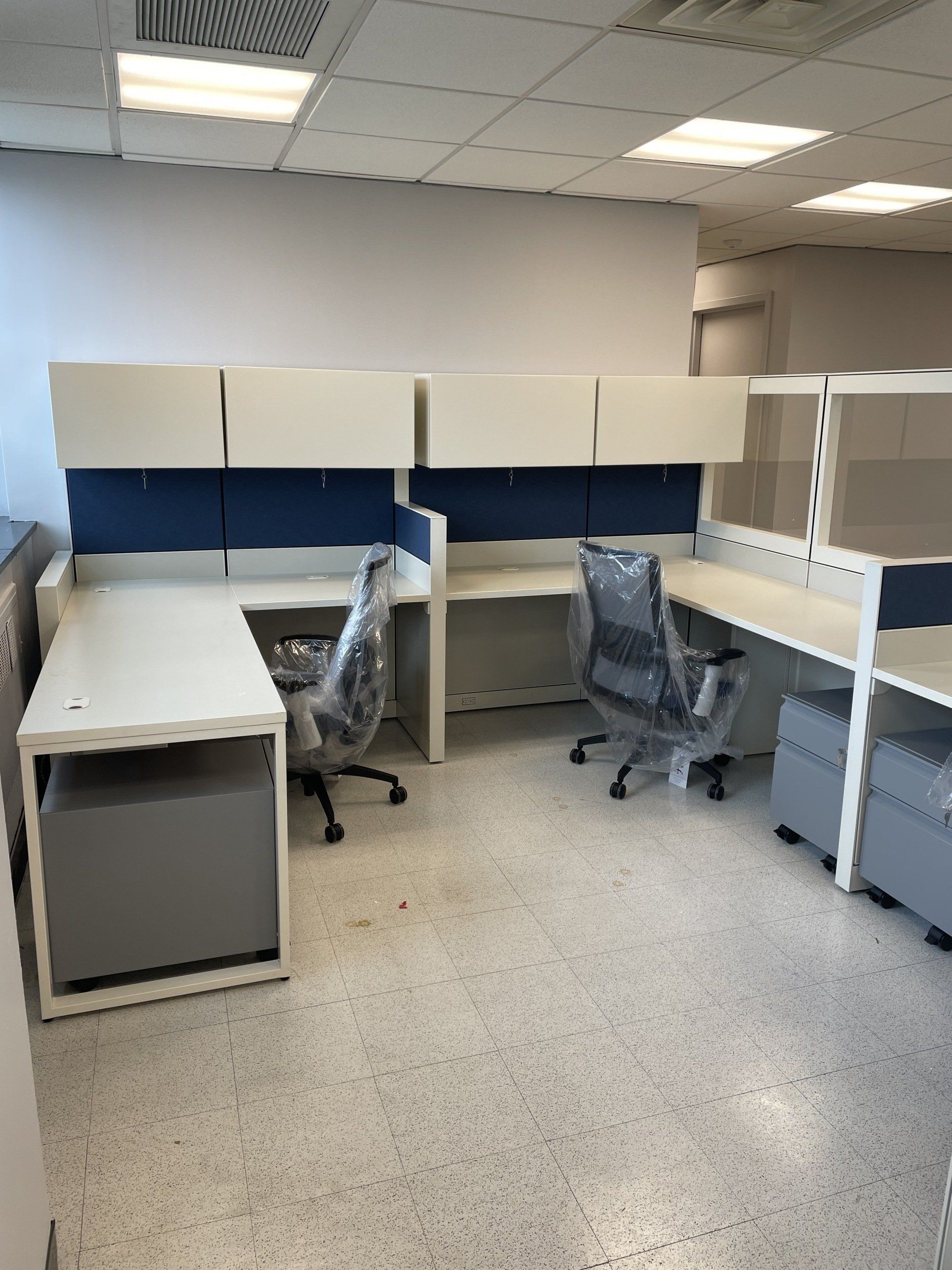 A cubicle with two desks and two chairs in it