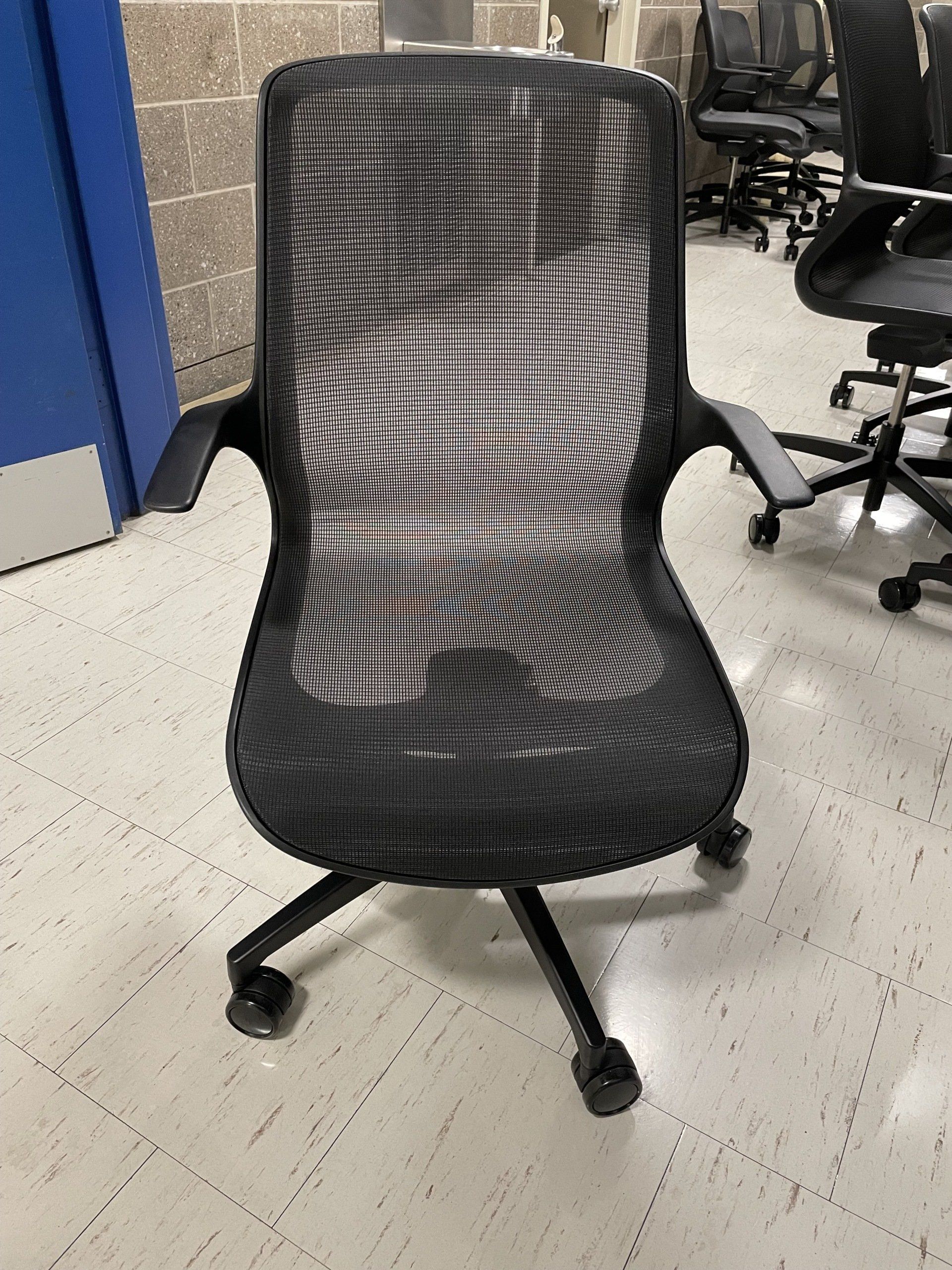 A black mesh office chair is sitting on a white tiled floor.