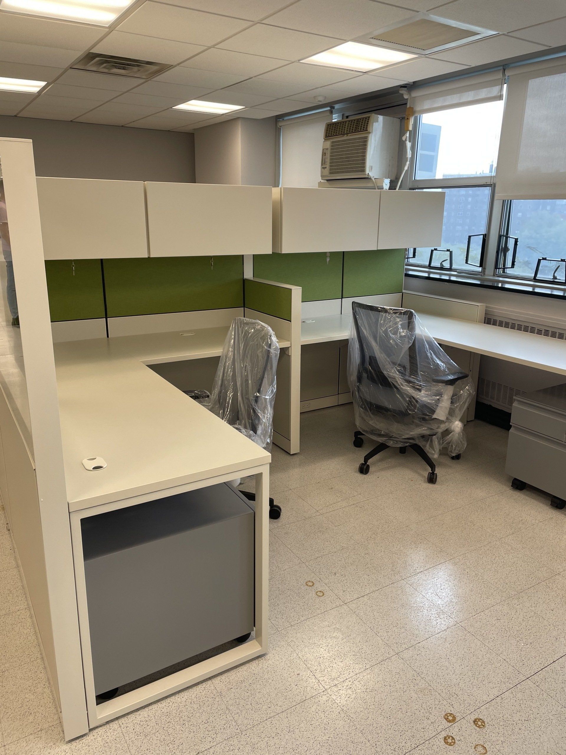 A cubicle with two desks and two chairs wrapped in plastic