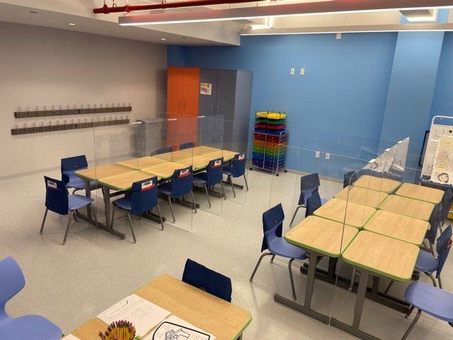 A classroom with tables and chairs and a stack of plastic chairs