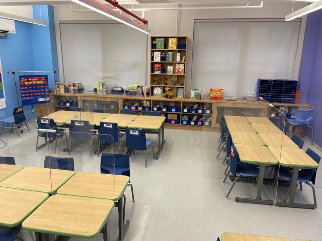 A classroom with tables and chairs and a shelf with books on it