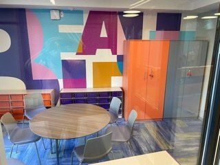 A room with a round table and chairs and a colorful mural on the wall.