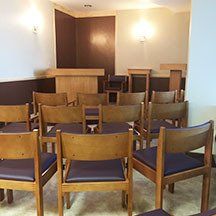 A row of wooden chairs in a room with a podium in the background.