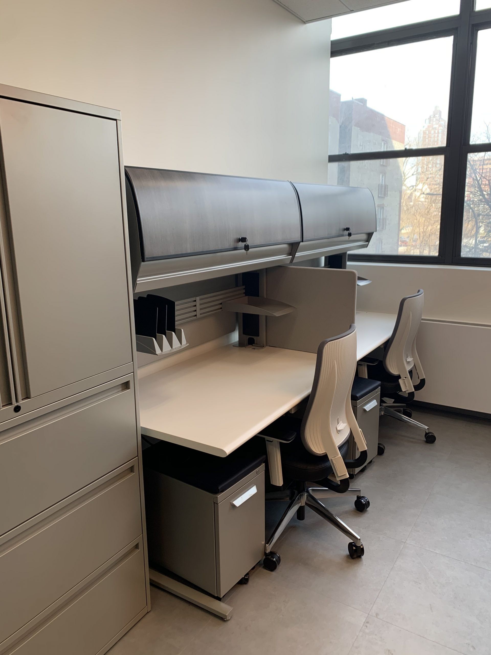 A room with two desks and two chairs in front of a window