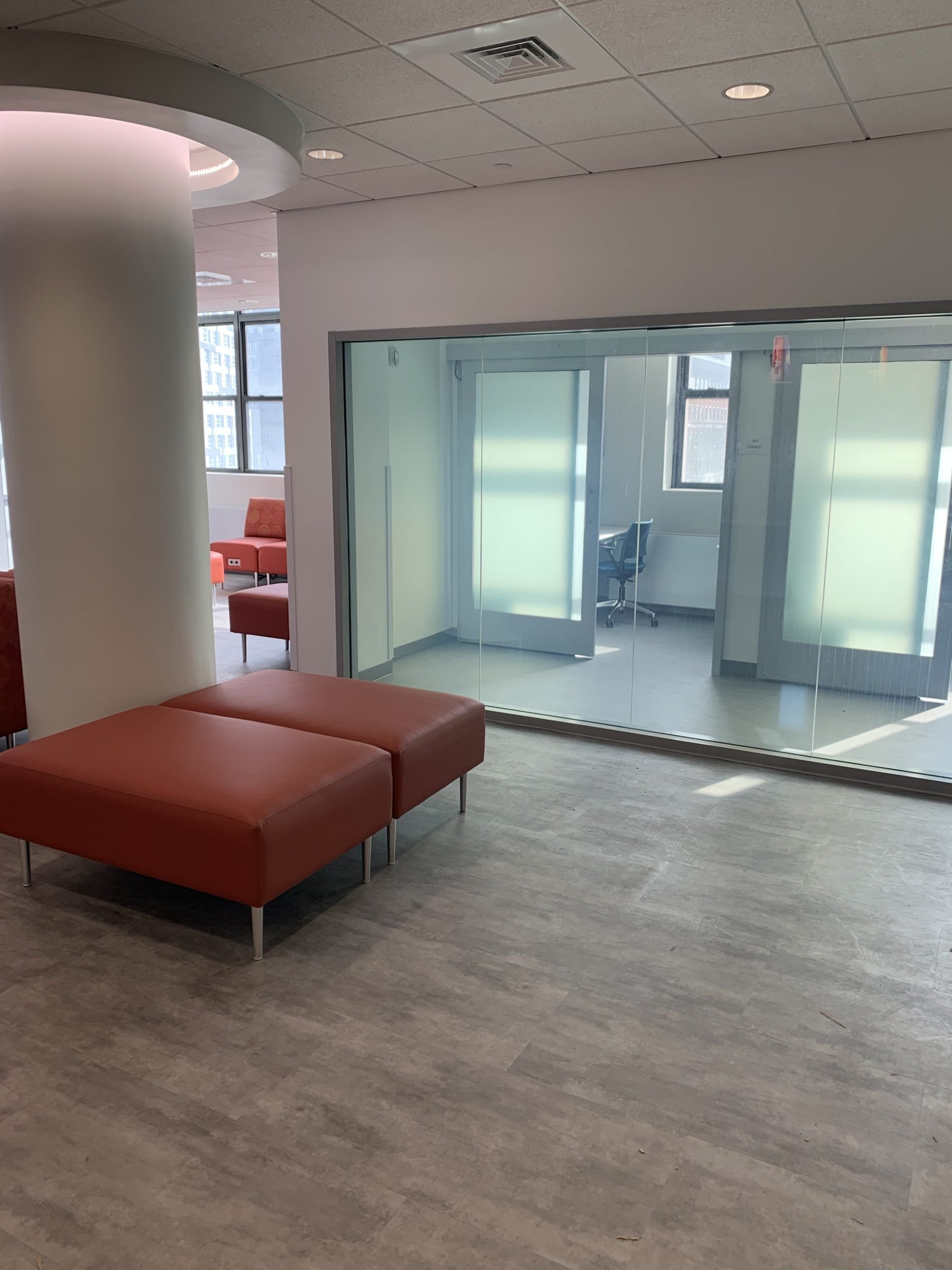 A waiting room with two red ottomans and a glass wall