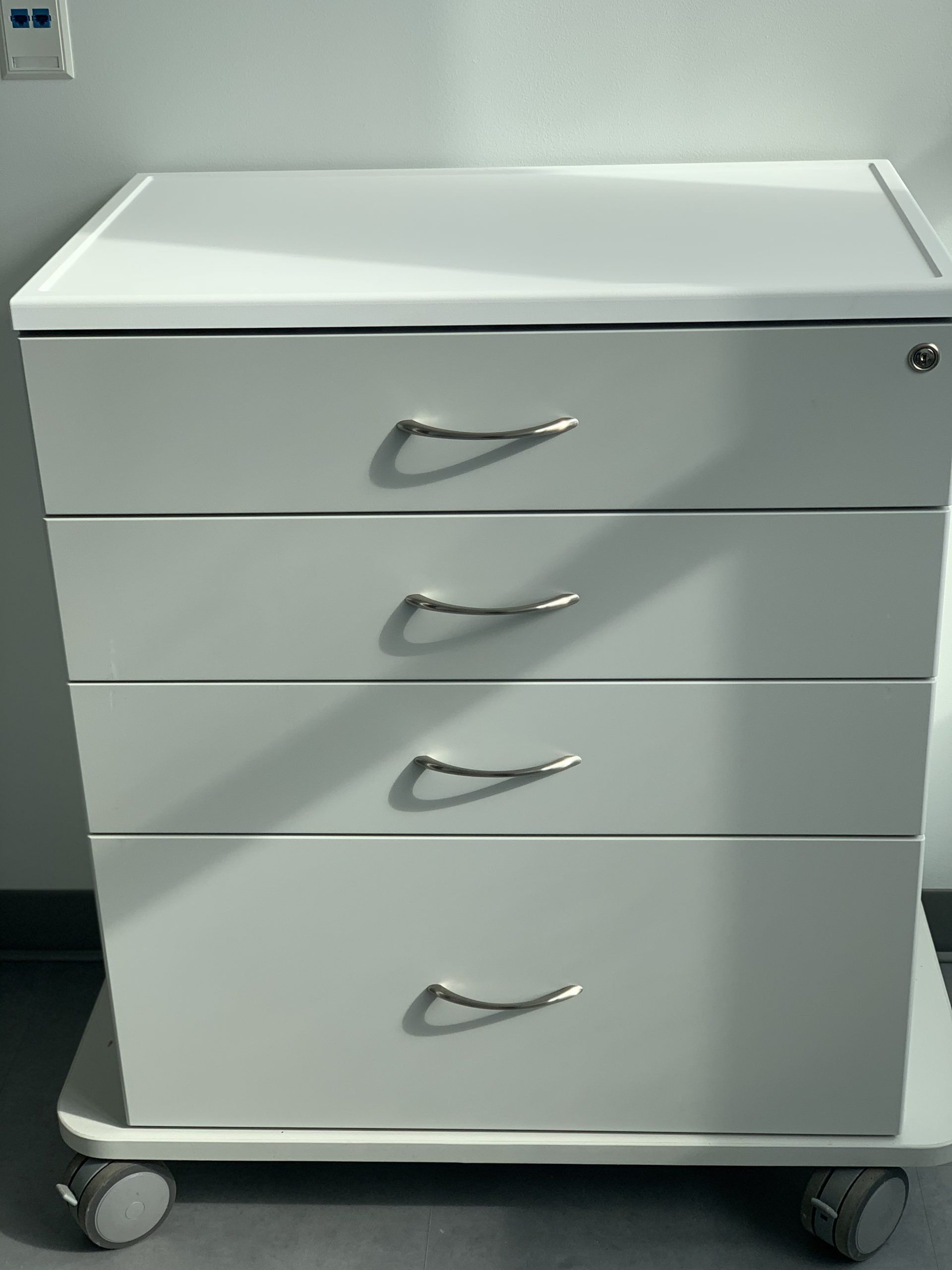 A white dresser with four drawers and wheels