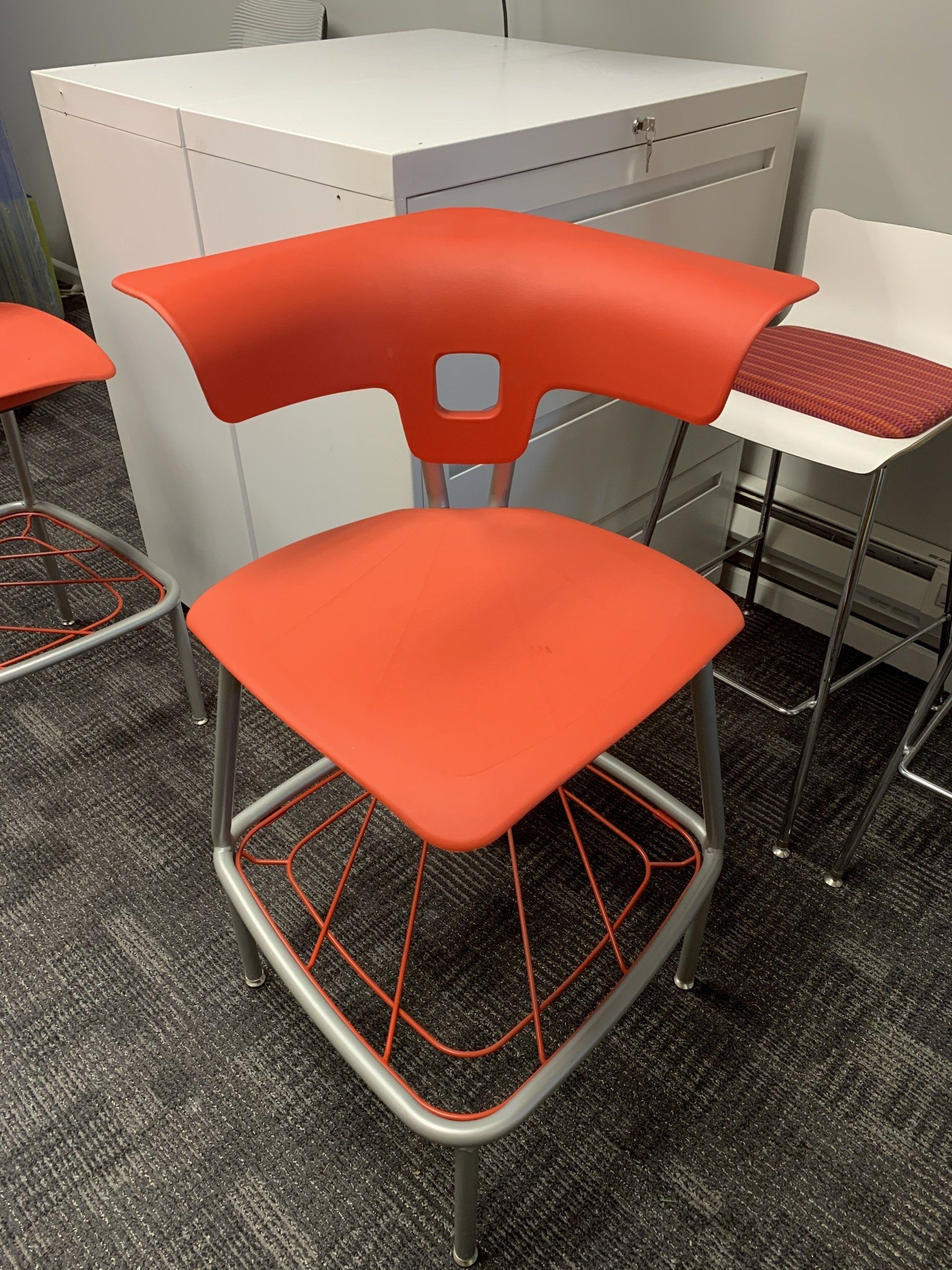A red chair in a room next to a white cabinet