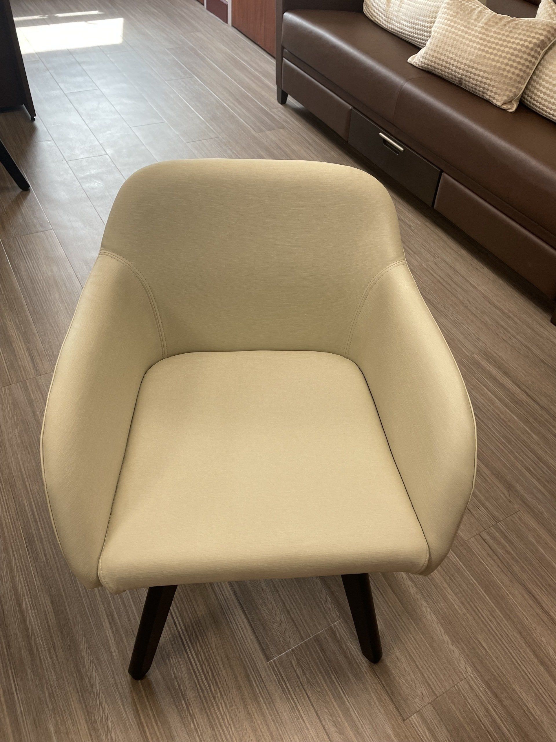 A white chair is sitting on a wooden floor next to a brown couch.