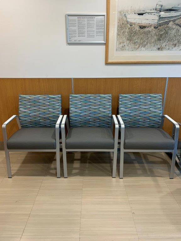 A row of chairs in a waiting room with a picture on the wall.
