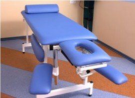 A blue massage table with a hole in the middle is in a room.