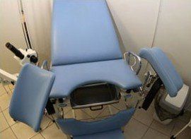 A blue gynecological chair is sitting in a room next to a microscope.