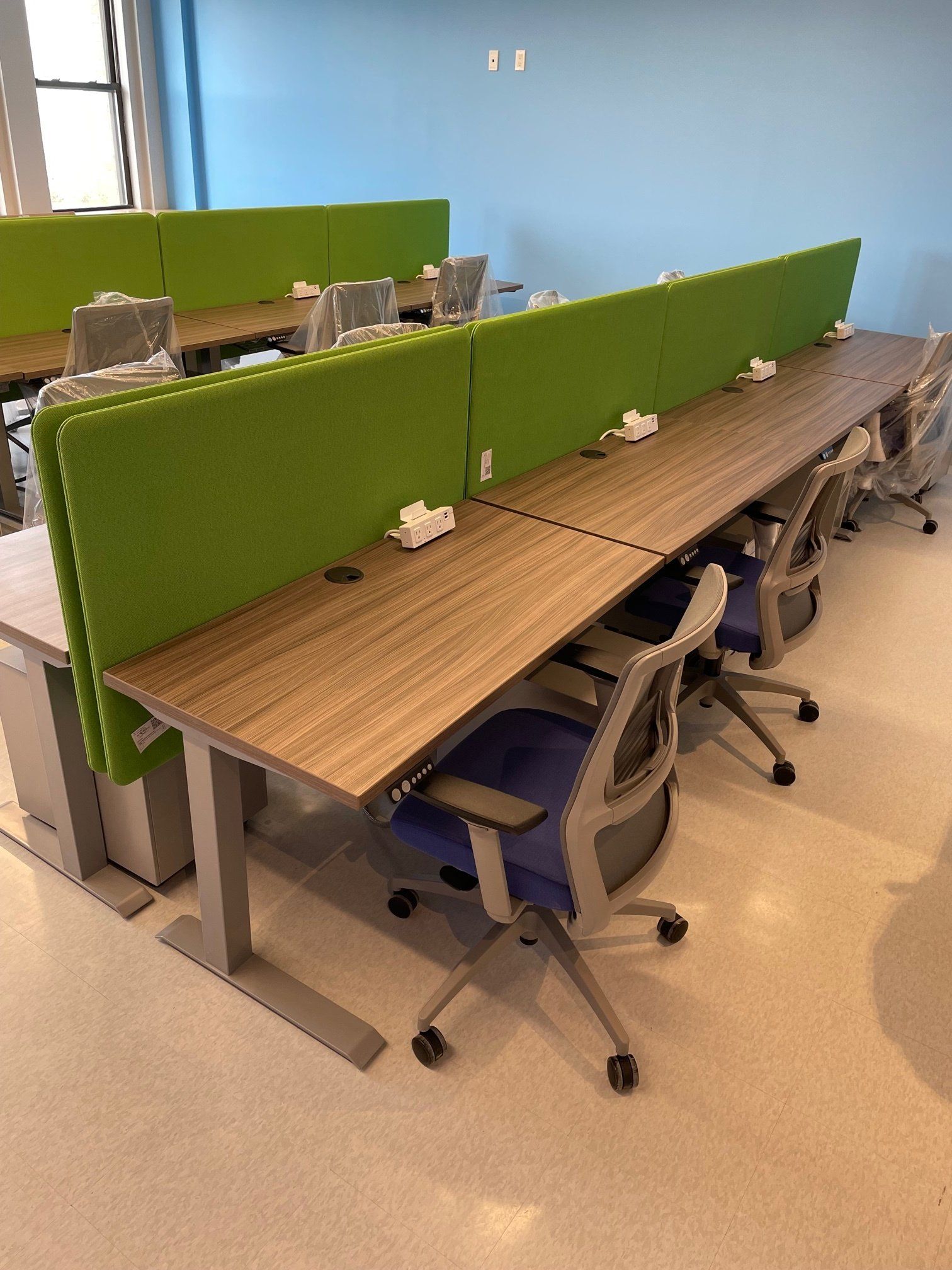 A row of wooden desks with green dividers and chairs in an office.