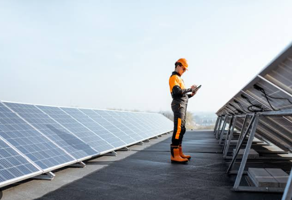 Worker in orange safety gear inspecting rooftop solar panels on a sunny day