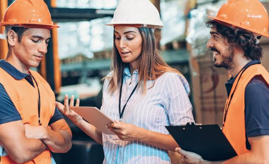 Three construction workers in hard hats reviewing plans on a tablet at a job site