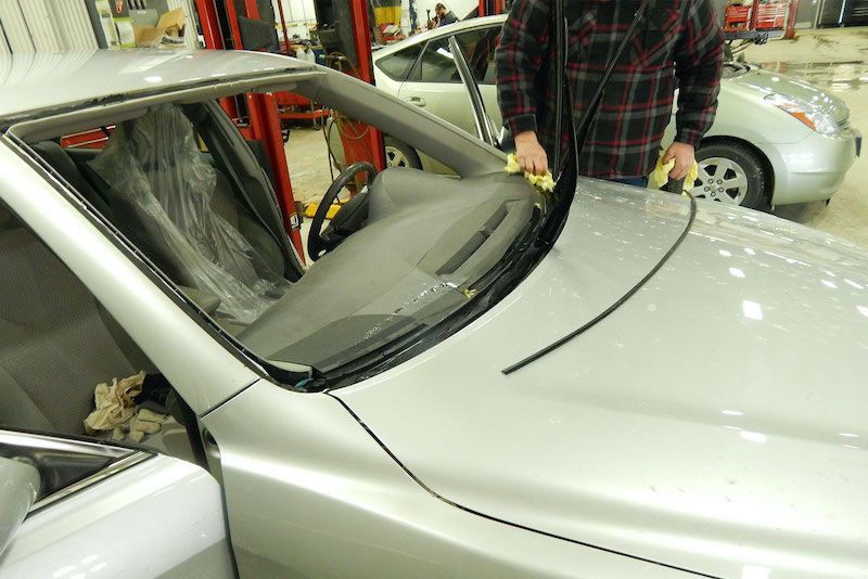 A man is cleaning the windshield of a silver car
