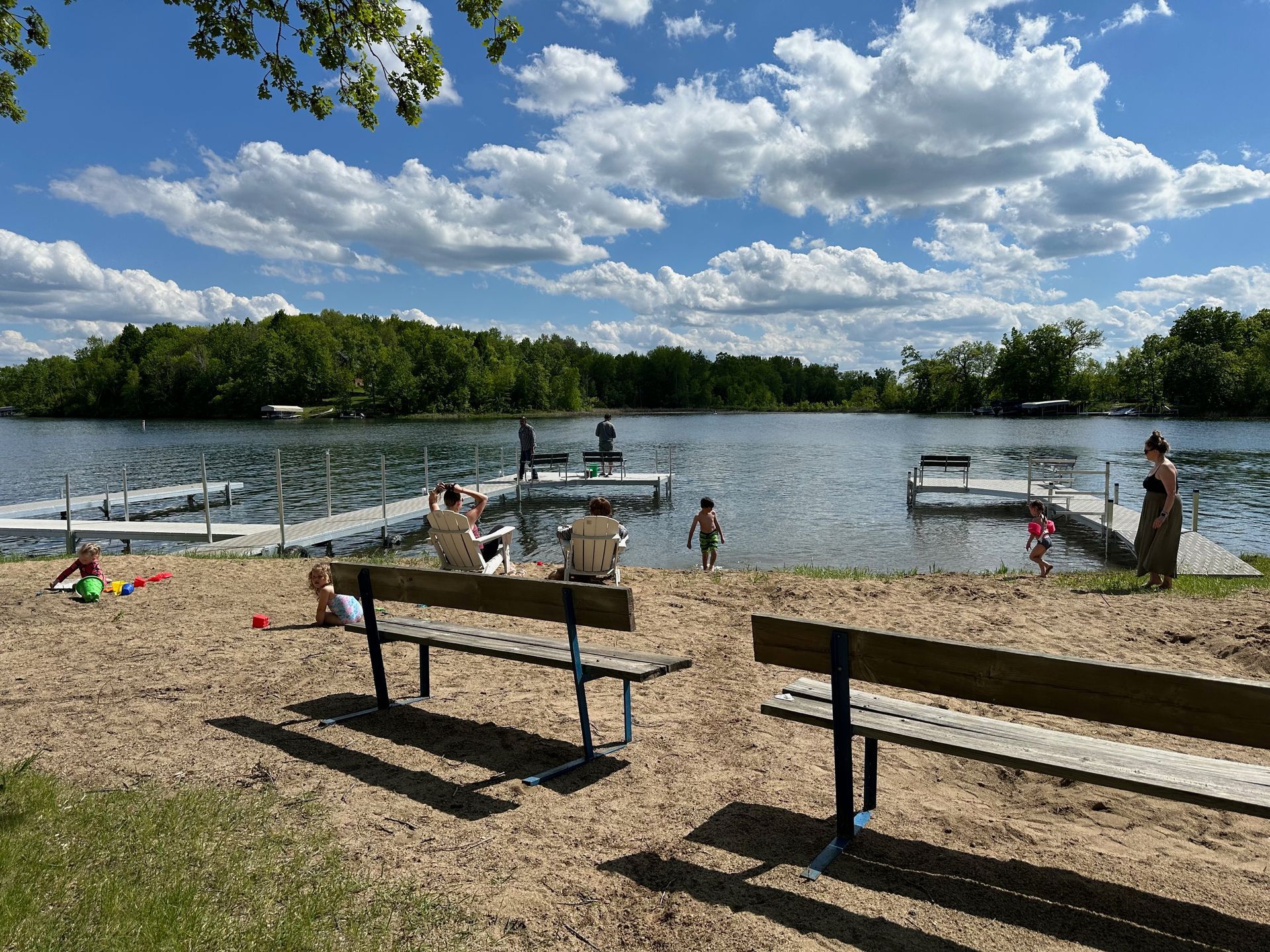 A couple of benches sitting on top of a sandy beach next to a lake.