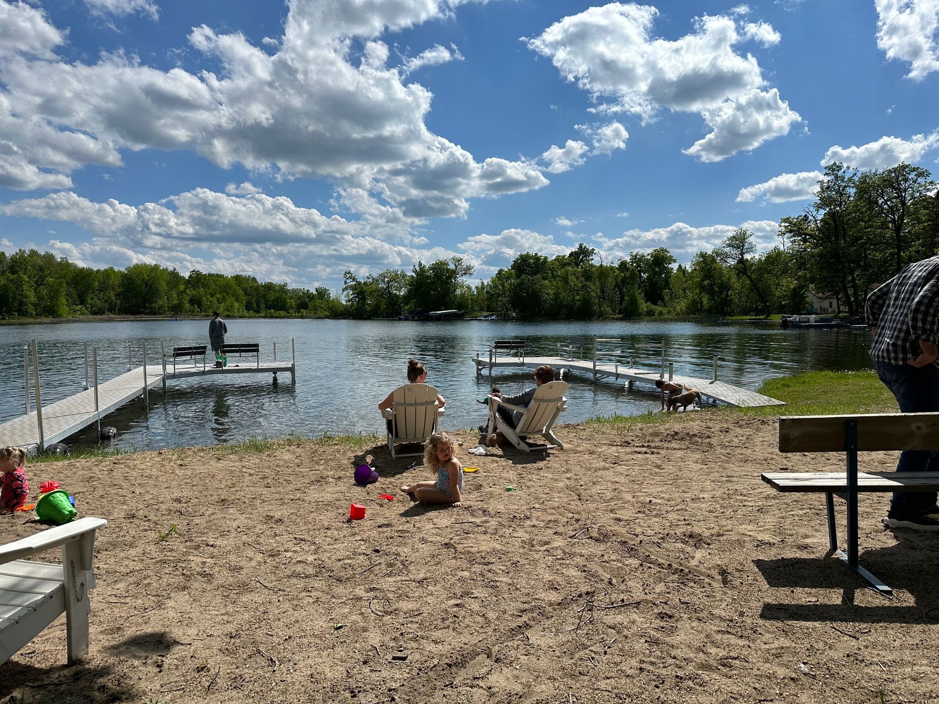 A group of people are sitting on a sandy beach near a lake.