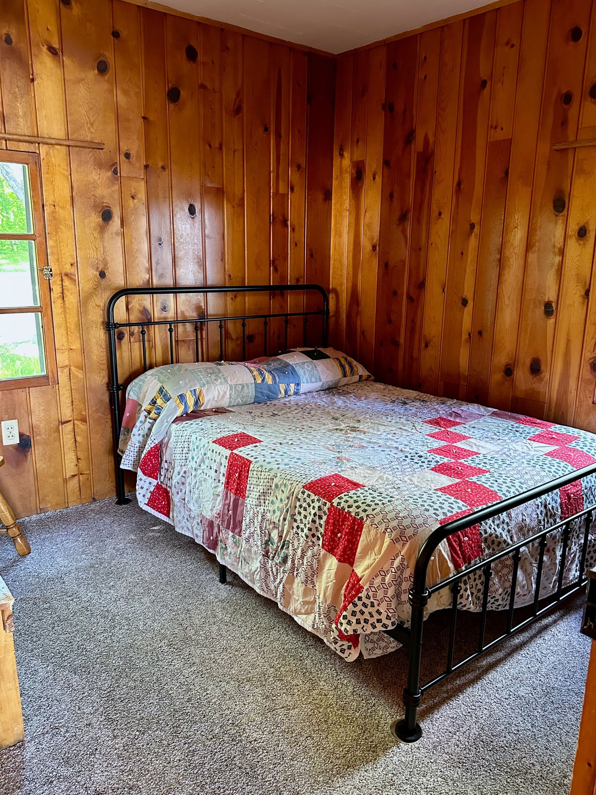 A bedroom with a bed , carpet , wooden walls and a window.