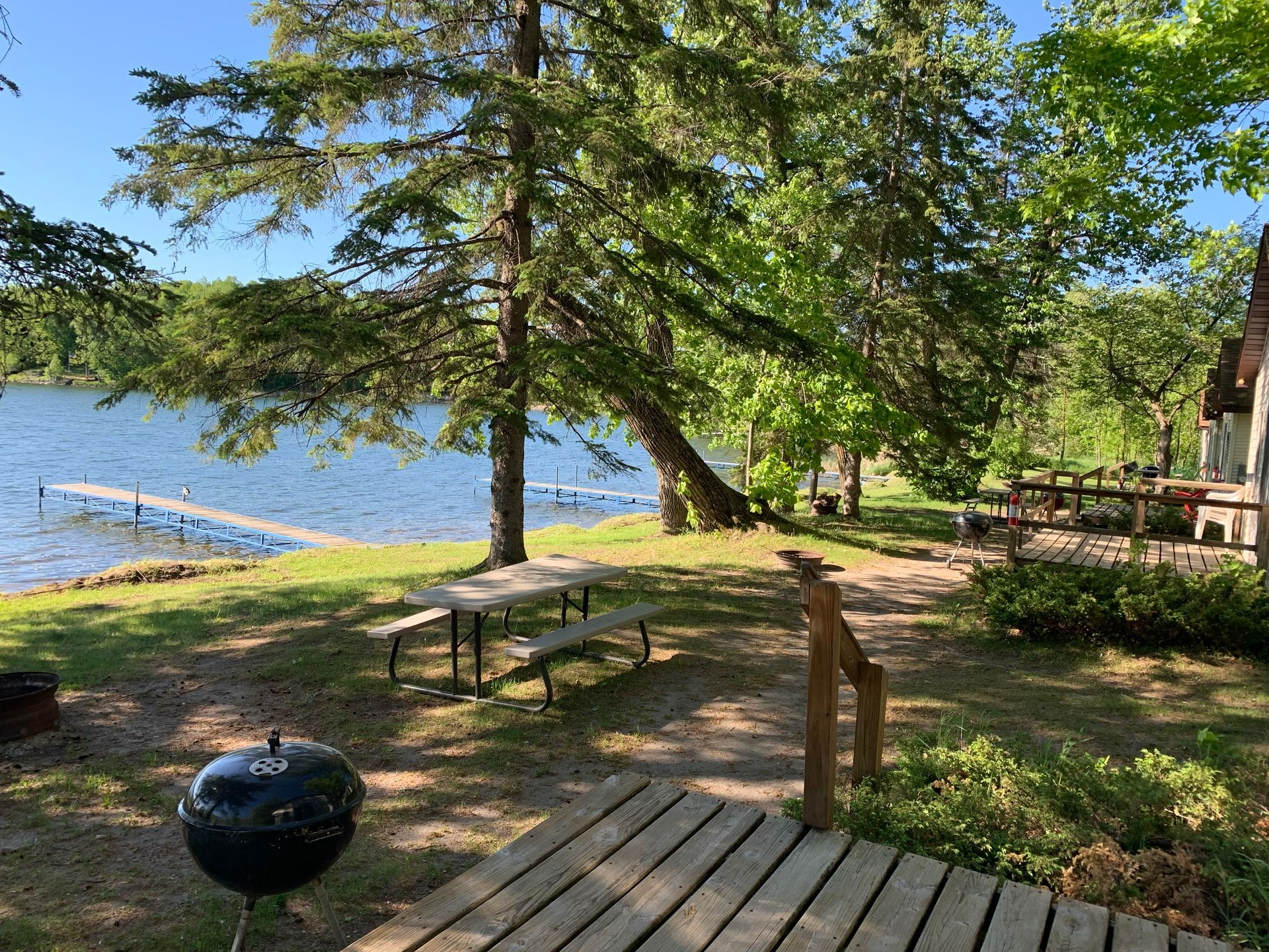 A picnic table and grill are sitting on a wooden deck next to a lake.