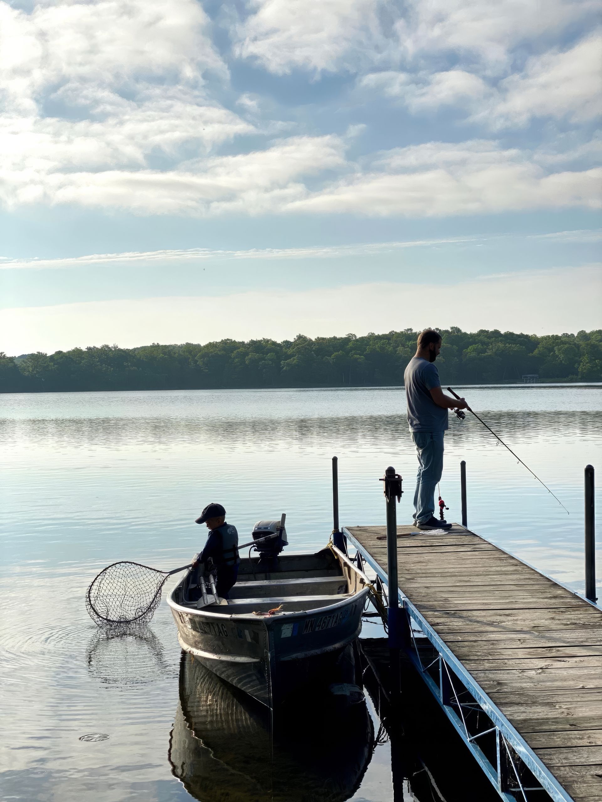 A man is fishing from a dock next to a boat
