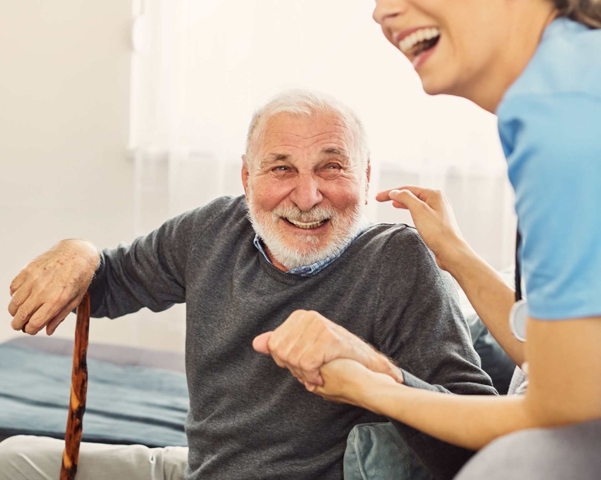 Older man with a cane smiling, being assisted by a person in blue.