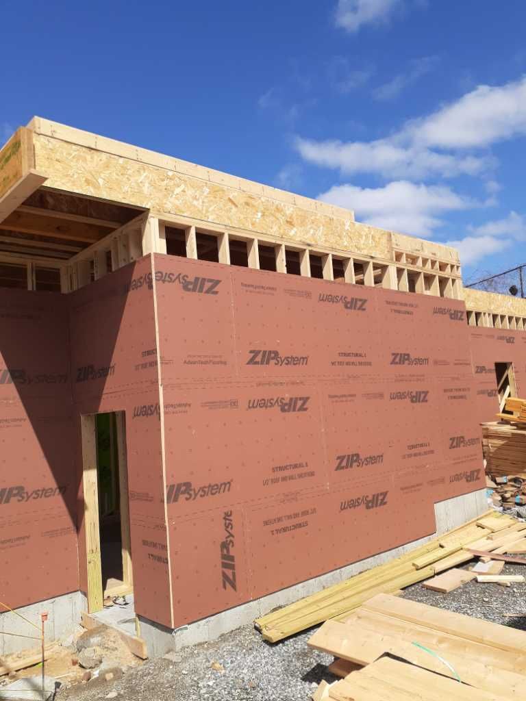 Construction of a building: wood framing with brown ZIP System sheathing and exposed roof. Blue sky.