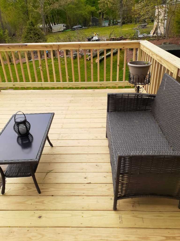 Wooden deck with brown wicker furniture, small black table, and a potted plant; overlooking a grassy yard.