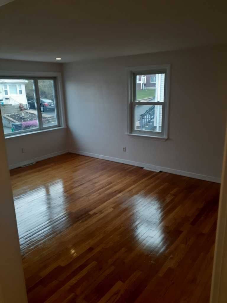 Empty room with hardwood floors, two windows, and white walls.