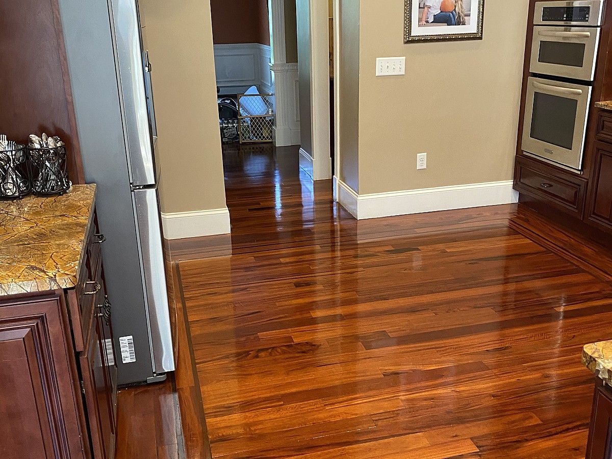 Shiny hardwood floors in a kitchen with wood cabinets, a stainless steel oven, and a hallway.