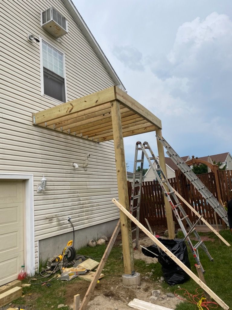 A partially constructed wooden deck attached to a light-colored house. Construction tools and ladders are visible.
