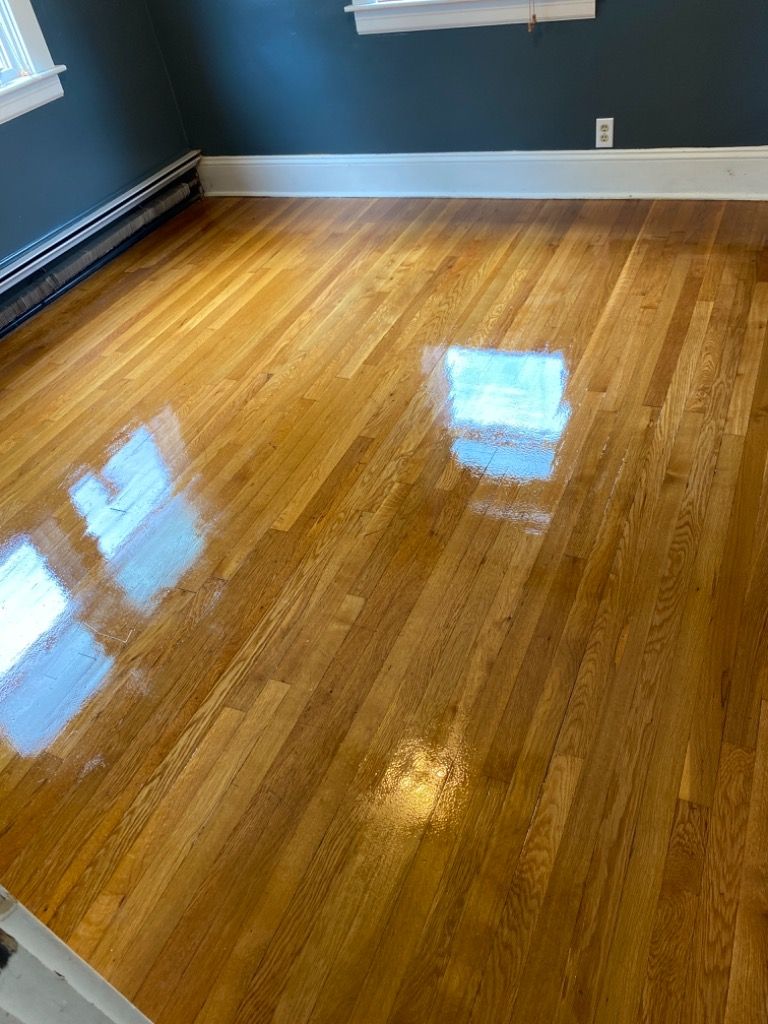 Newly refinished, shiny hardwood floor reflecting window light in a room with blue walls and white trim.