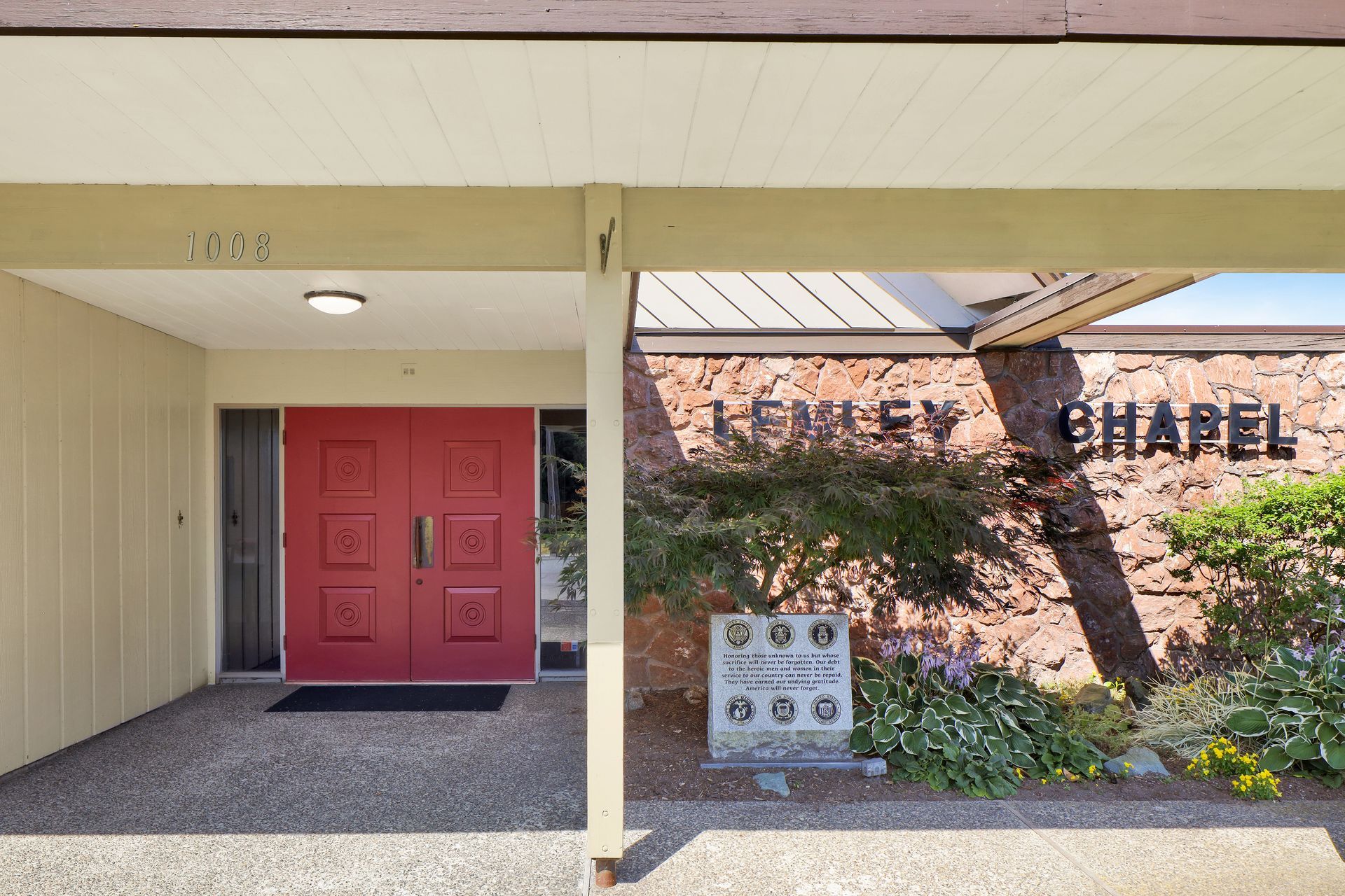 Entrance to a building with red double doors, covered walkway, and a brick wall marked “CHAPEL.”