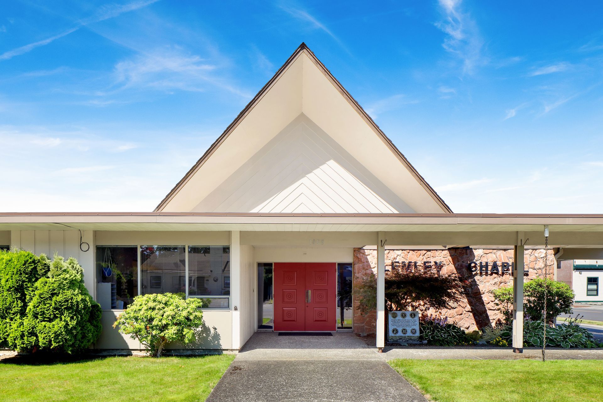 Front view of a small building with a red door, white trim, and a peaked roof under a blue sky