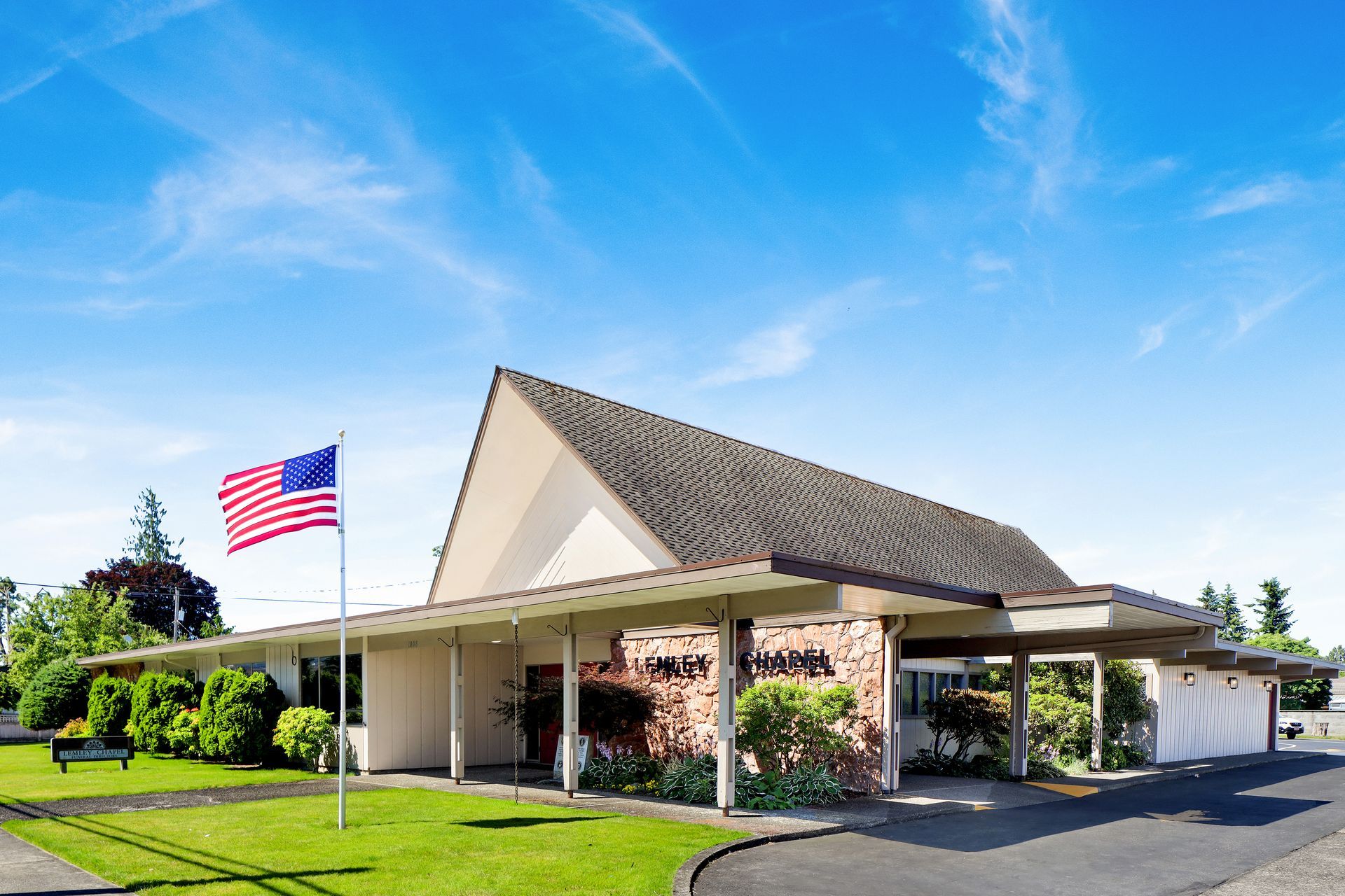 Small brick building with a covered entrance and an American flag flying on a sunny day